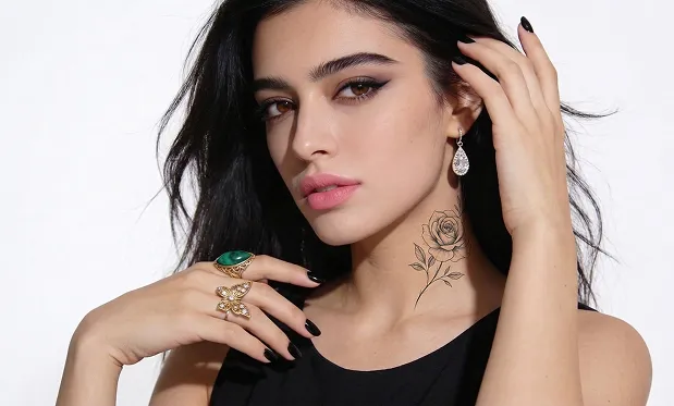 تُلتقط الصورة من زاوية أوسع تُظهر المزيد من الجزء العلوي من جسم الشخص، والشخص يتخذ وضعية بيد تلمس شعره، مما يكشف عن وشم على رقبته.